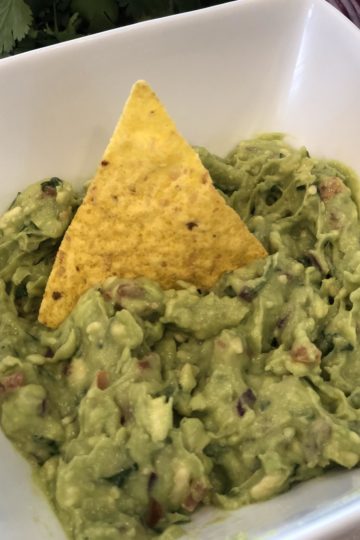 Bowl of homemade guacamole with a tortilla chip in the center