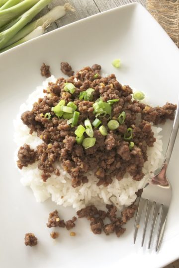 Fast & Easy Korean Beef with Rice on a plate with a fork and served with rice ad green onions on top.