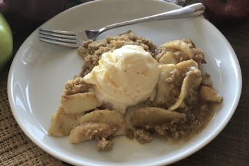 the BEST Apple crisp on a plate with a fork and apples in the background