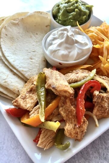Easy Sheet Pan Chicken Fajitas served with flour tortillas, peppers, onions, sour cream and guacamole