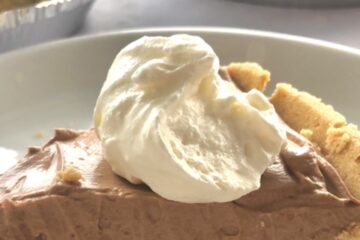 A slice of easy chocolate cream pie with homemade whipped cream on top in a graham cracker crust