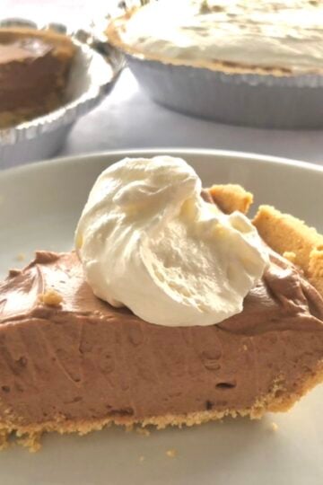A slice of easy chocolate cream pie with homemade whipped cream on top in a graham cracker crust