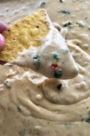 fresh homemade queso cheese dip and a yellow corn tortilla chiip dipped into the cheese dip