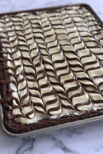 Close up shot of a sheet pan full of brownies with cream cheese frosting and a chocolate drizzle on top