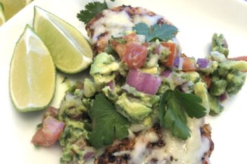 Grilled Chicken with avocado salsa on a white plate for serving with cilantro and limes for garnish