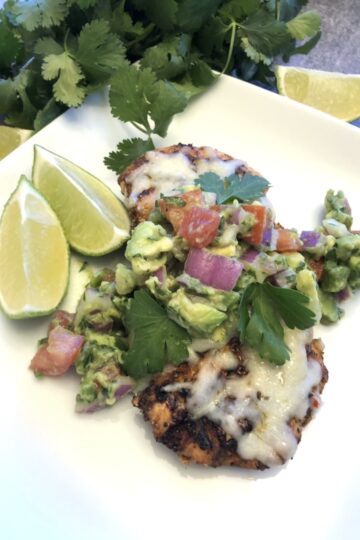 Grilled Chicken with avocado salsa on a white plate for serving with cilantro and limes for garnish