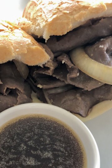 thin sliced roast beef and onions in a soft hoagie bun for an easy French dip sandwich with a side of au jus sauce for dipping