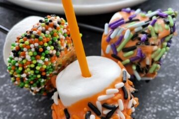 Three Halloween Marshmallow pops next to a plate of marshmallow pops