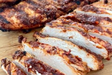 Grilled Chipotle Chicken on a wooden cutting board with full pieces of chicken and chicken cut up into bite sized pieces.