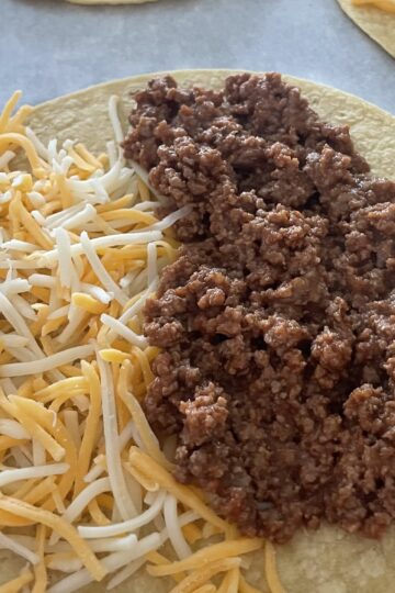 Taco Meat on a corn tortilla with grated cheese to make tacos