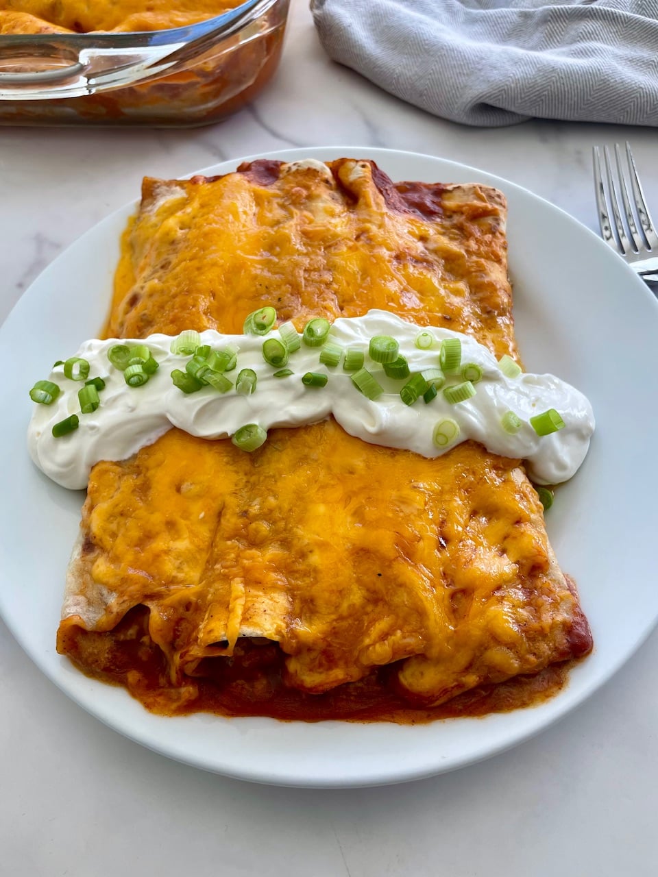 A plate of ground beef enchiladas topped with sour and green onoins.